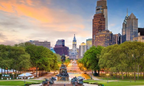 a park with a fountain and trees with buildings in the background